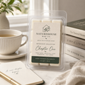 Clear clamshell package of Chapter One Wax Melts by Naturehouse Wax Company placed on a cozy tabletop setting with books, a notebook, and a cup of tea in the background.