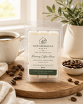 Hand-poured Morning Coffee House Wax Melts by Naturehouse Wax Company on a wooden tray surrounded by coffee beans, a cup of coffee, and a green plant in soft natural light.