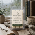 Rainy Reading Room Wax Melts in clear packaging displayed on a cozy wooden surface near a rainy window, surrounded by books, a cup, and a knitted blanket.
