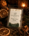 Orange Clove Hearth Wax Melts package displayed on a wooden surface surrounded by dried orange slices, whole cloves, cinnamon sticks, pinecones, and warm candlelight, evoking a cozy, natural atmosphere.